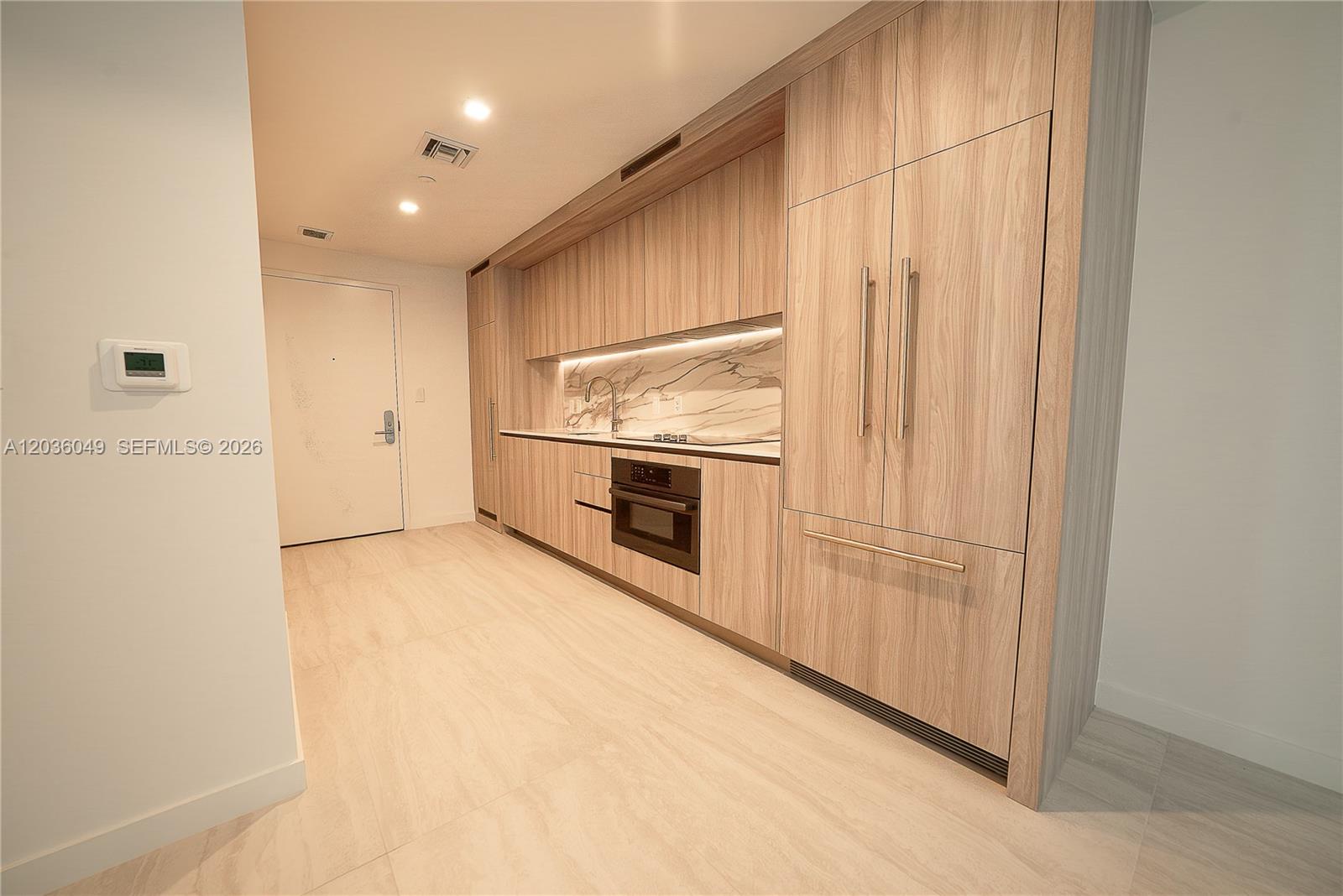 A modern kitchen features light wood cabinetry, integrated appliances, and a marble-patterned backsplash — 77 SE 5TH ST # 1607, Miami FL 33131, MIAMI, FL