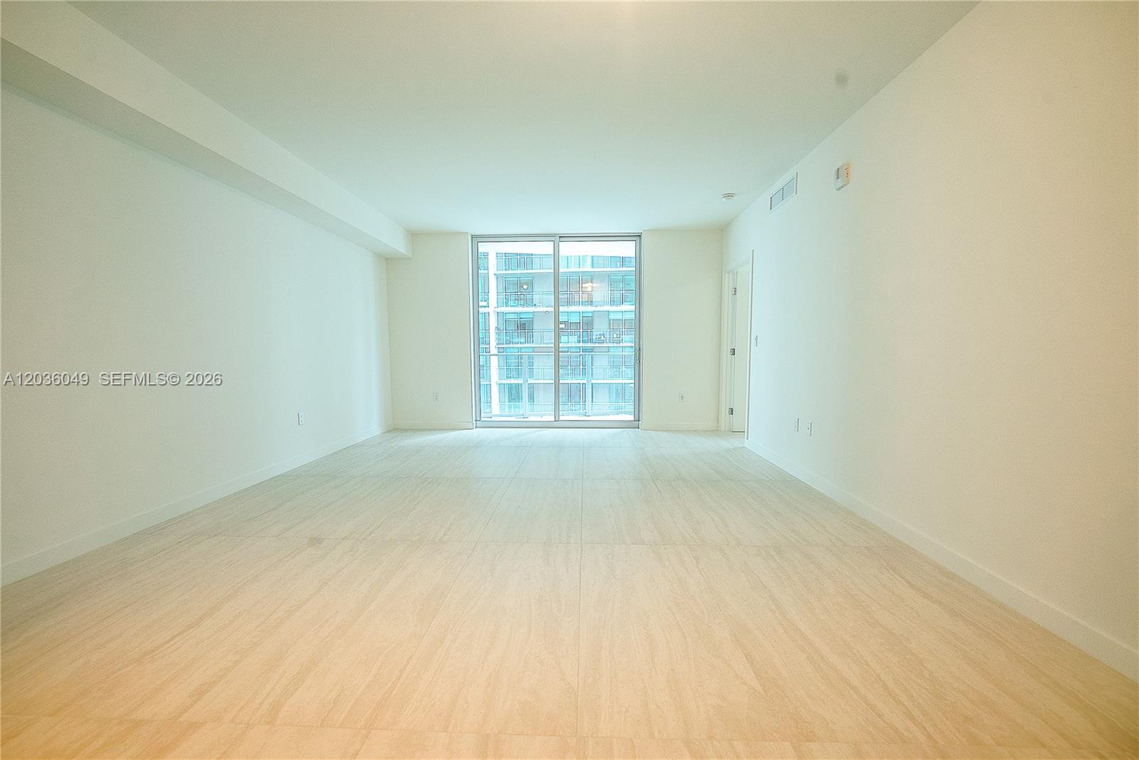 An empty room features light-colored tile flooring, white walls, and a large sliding glass door — 77 SE 5TH ST # 1607, Miami FL 33131, MIAMI, FL