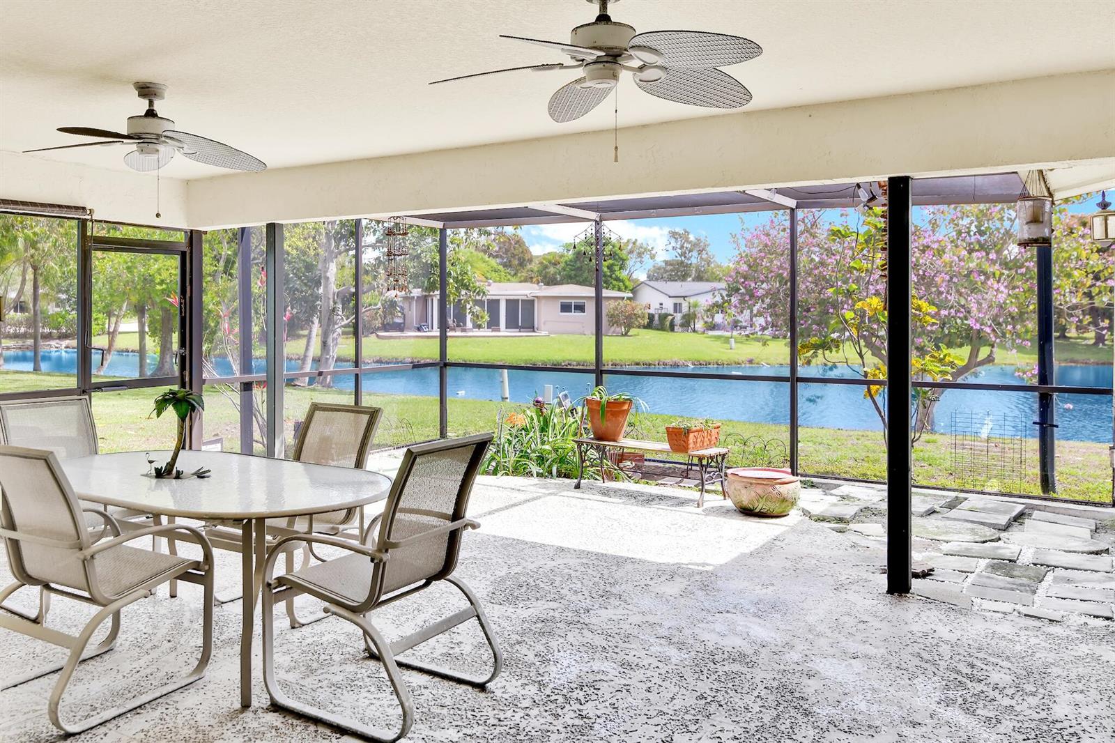 A screened-in patio features a dining set, two ceiling fans, and views of a lake — 14592 Country Side Lane, Delray Beach FL 33484, DELRAY BEACH, FL