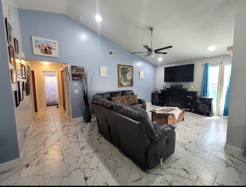A living room with vaulted ceilings, marble-look tile flooring, a black leather sofa, and television — 2609 MILL RUN BOULEVARD, KISSIMMEE, FL