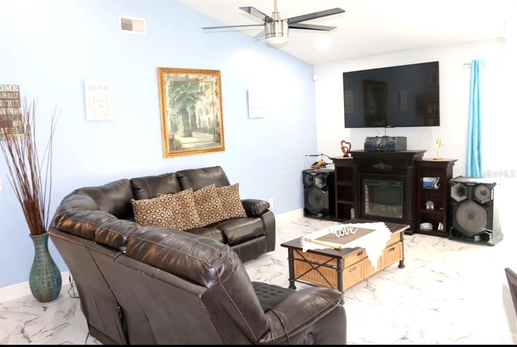 A living room features a dark leather sofa, a fireplace with a television, and tile flooring — 2609 MILL RUN BOULEVARD, KISSIMMEE, FL