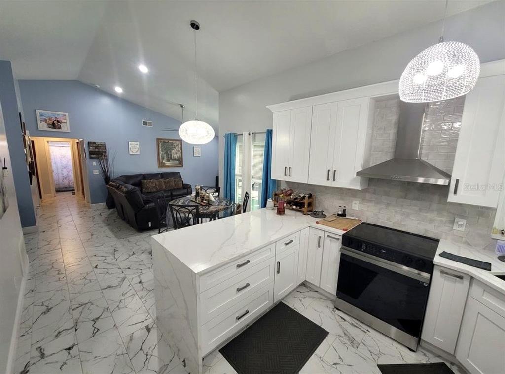 A kitchen with white cabinets and marble-patterned countertops overlooks a living room with tiled floors — 2609 MILL RUN BOULEVARD, KISSIMMEE, FL