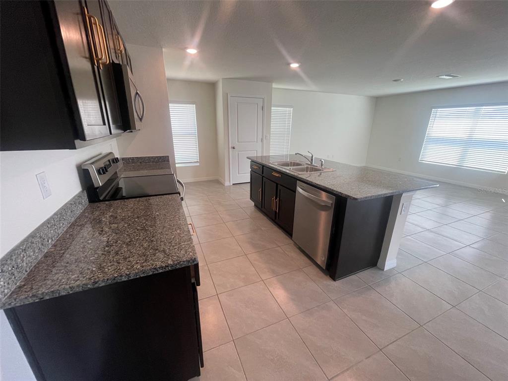 A kitchen features dark cabinets, granite countertops, stainless steel appliances, and light tile flooring — 35288 SPRUCE KNOB COURT, DADE CITY, FL
