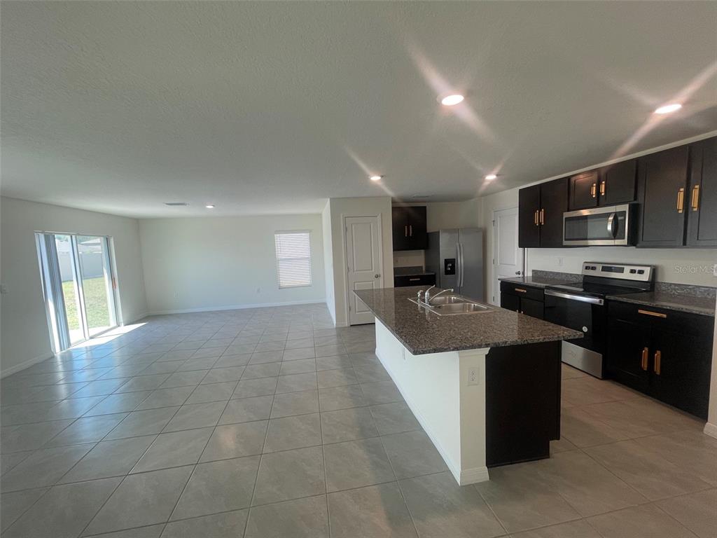A kitchen with dark cabinets and a granite island opens to a tiled living area — 35288 SPRUCE KNOB COURT, DADE CITY, FL