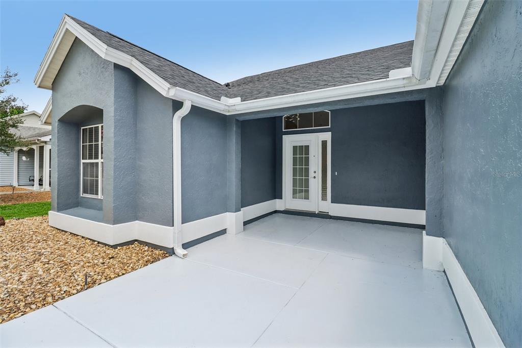 A covered concrete entryway leads to a white double door on a blue house — 207 DESOTA COURT, THE VILLAGES, FL