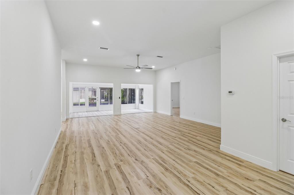 An empty living room features light wood-look flooring, white walls, and a glass-enclosed patio area — 207 DESOTA COURT, THE VILLAGES, FL