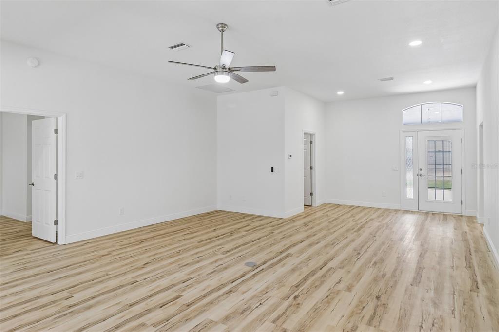 An empty room with white walls, light wood-look flooring, a ceiling fan, and a front door — 207 DESOTA COURT, THE VILLAGES, FL