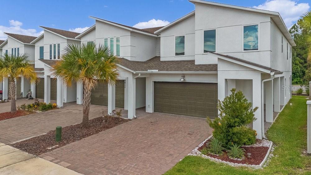 A multi-story townhouse exterior features white stucco walls, a brown shingle roof, and paved driveways — 3401 BEAU ROAD, KISSIMMEE, FL