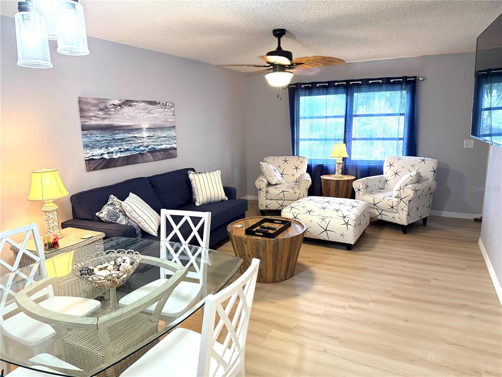A living and dining area features a blue sofa, two patterned armchairs, and light flooring — 390 301 BOULEVARD W UNIT 1B, BRADENTON, FL