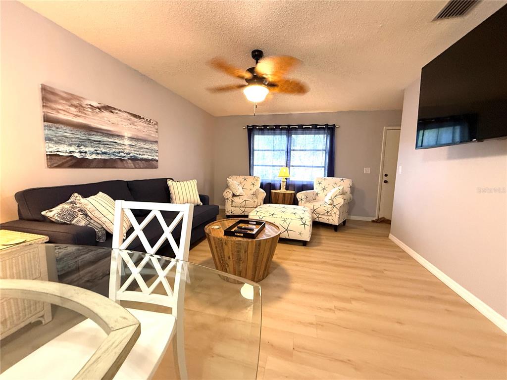 A living room features a dark sofa, two patterned armchairs, a wooden coffee table, and flooring — 390 301 BOULEVARD W UNIT 1B, BRADENTON, FL