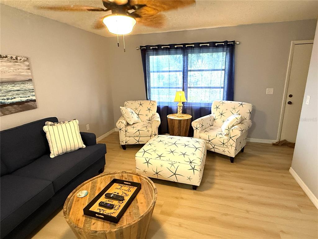 A living room features a blue sofa, two patterned armchairs, an ottoman, and light flooring — 390 301 BOULEVARD W UNIT 1B, BRADENTON, FL
