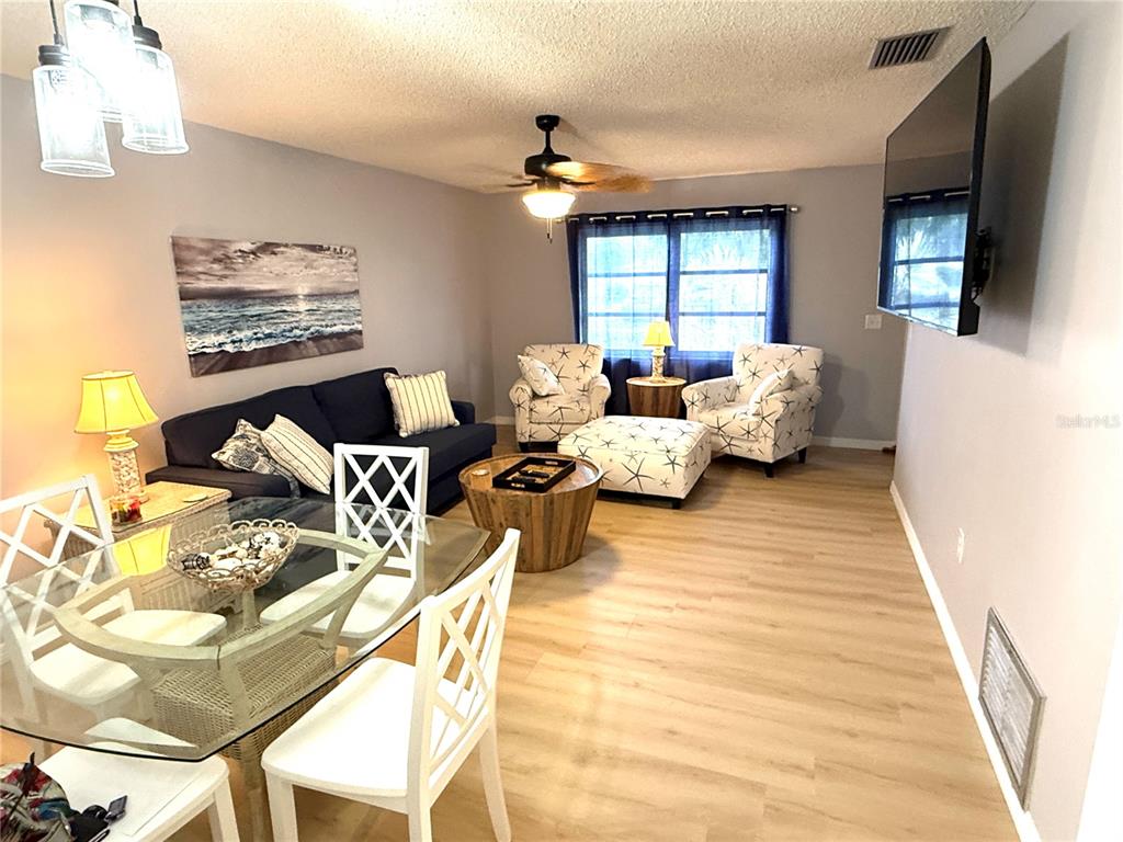 A living room and dining area feature light wood flooring, a ceiling fan, and furniture — 390 301 BOULEVARD W UNIT 1B, BRADENTON, FL