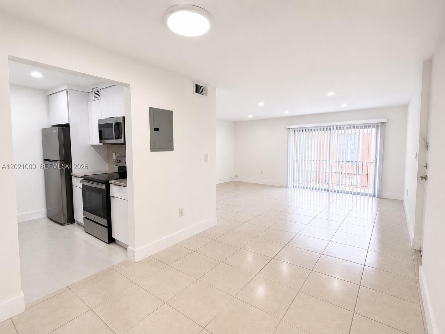 A kitchen with stainless steel appliances opens into a bright, tiled living area with balcony access — 7160 Fairway Dr # J16, Miami Lakes FL 33014, MIAMI LAKES, FL