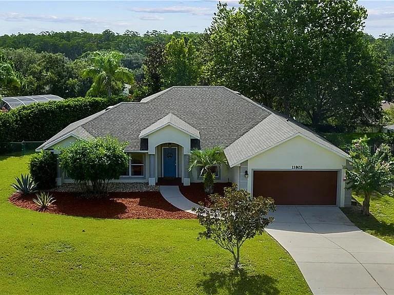 A single-story house with a gray shingled roof, a blue front door, and a garage — 11802 GRAND HILLS BOULEVARD, CLERMONT, FL