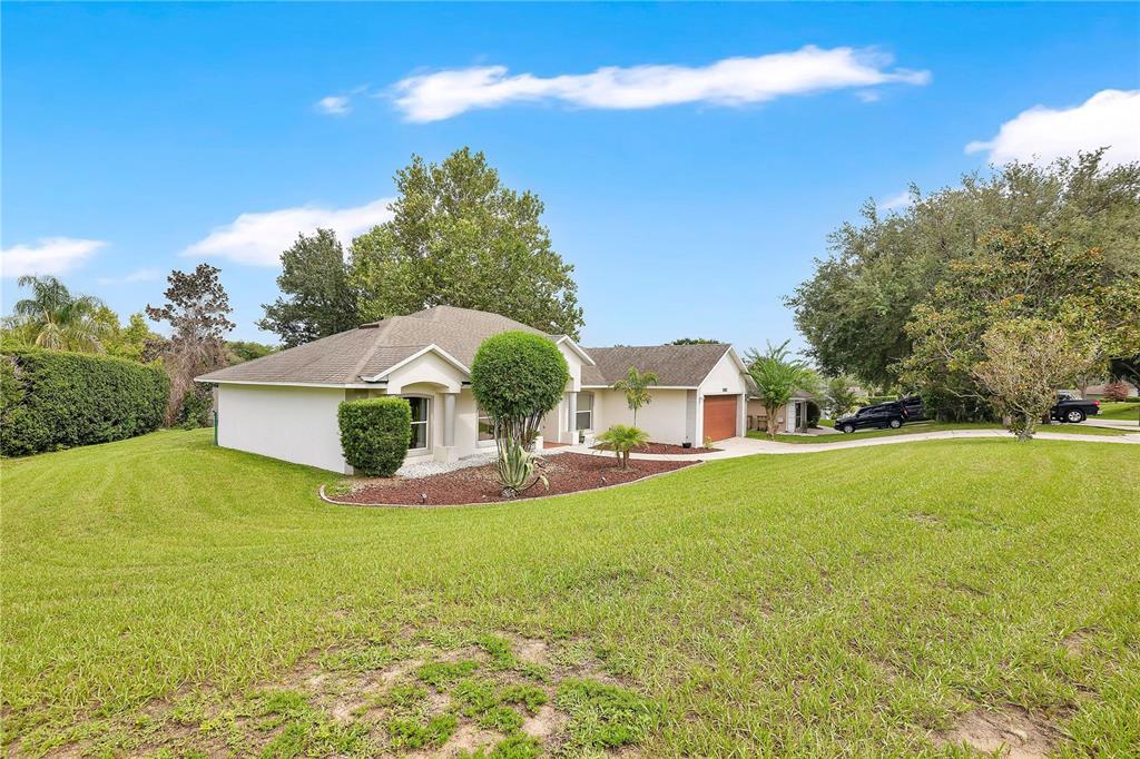 A single-story house with a tan exterior, a brown roof, and a large front lawn — 11802 GRAND HILLS BOULEVARD, CLERMONT, FL