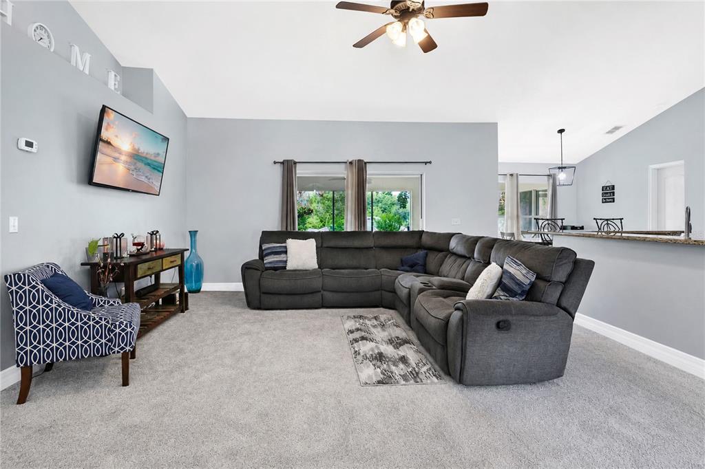A living room features gray carpet, a large sectional sofa, and a wall-mounted television — 11802 GRAND HILLS BOULEVARD, CLERMONT, FL