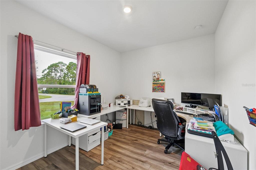 A home office features white walls, wood-look flooring, a large window, and an L-shaped desk — 4476 BLACKMAN STREET, NORTH PORT, FL