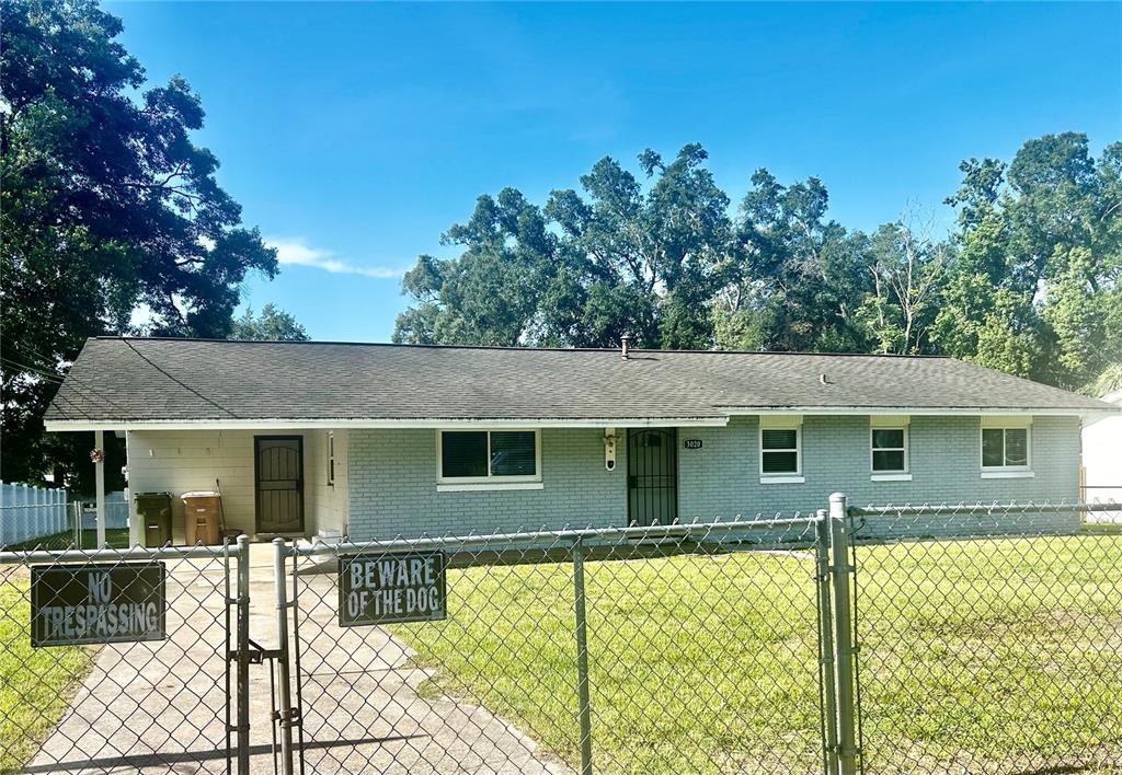 A single-story gray brick house sits behind a chain-link fence with warning signs — 3020 SE 11TH STREET, OCALA, FL