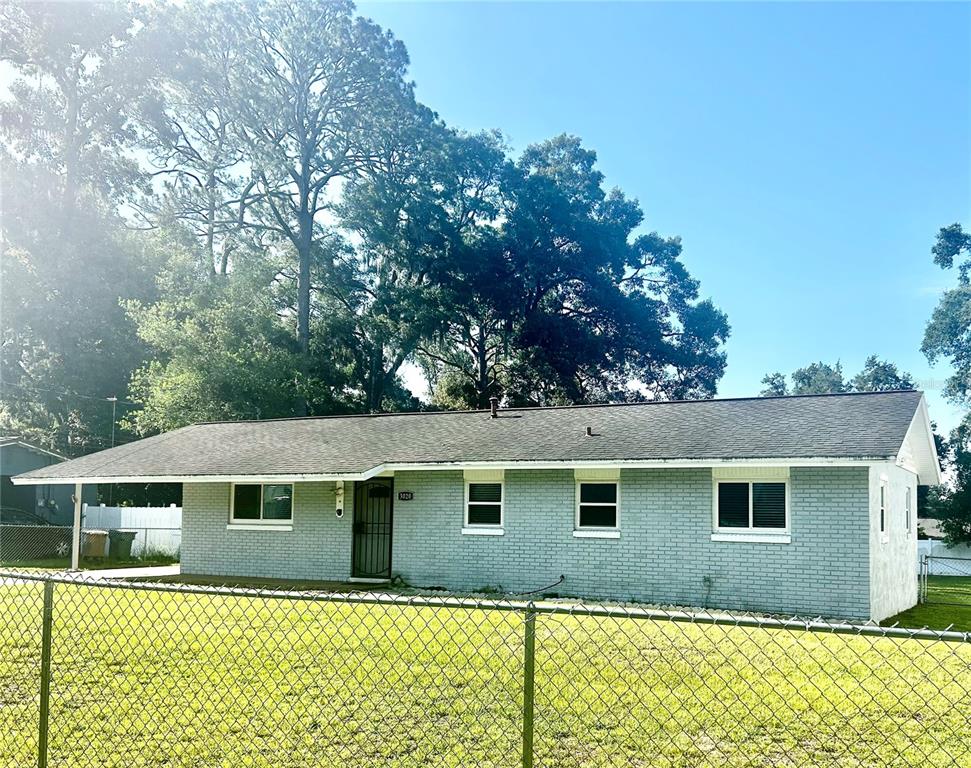 A single-story gray brick house with a carport sits behind a chain-link fence — 3020 SE 11TH STREET, OCALA, FL