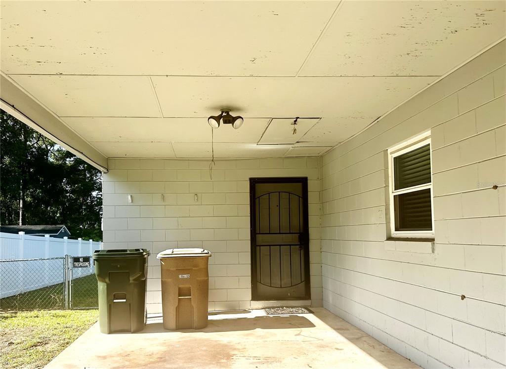 A covered concrete patio features a metal screen door, two trash bins, and block walls — 3020 SE 11TH STREET, OCALA, FL