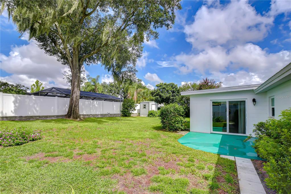 A backyard with a green patio, a large tree, and a white privacy fence — 2205 MALIBU DRIVE, BRANDON, FL