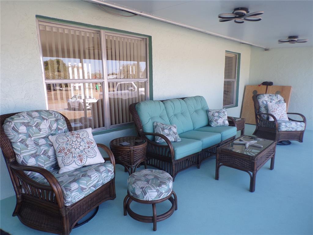 A covered patio features wicker furniture with teal cushions and a matching patterned armchair — 27097 OMNI LANE, PUNTA GORDA, FL