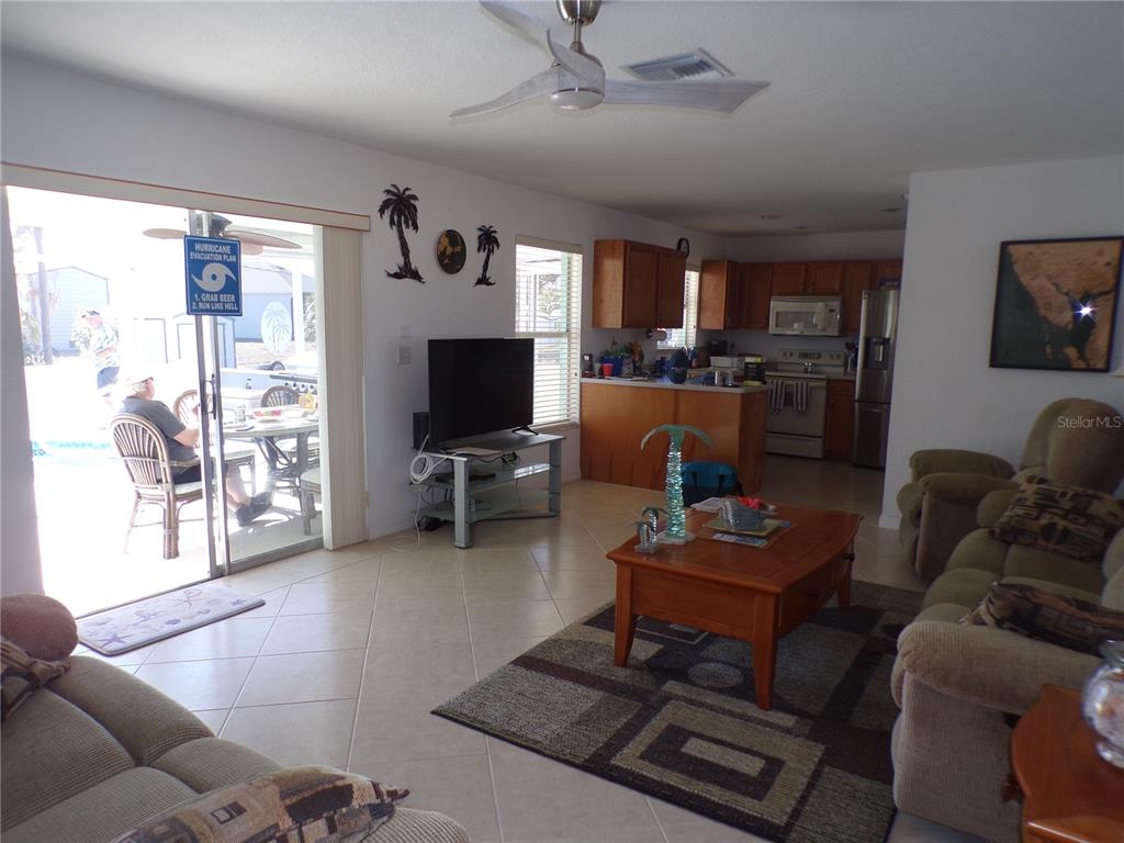 An open-concept living room and kitchen with tile flooring, a ceiling fan, and sliding doors — 27097 OMNI LANE, PUNTA GORDA, FL