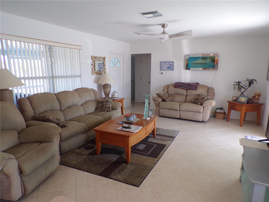 A living room features beige furniture, a wooden coffee table, tile flooring, and a ceiling fan — 27097 OMNI LANE, PUNTA GORDA, FL