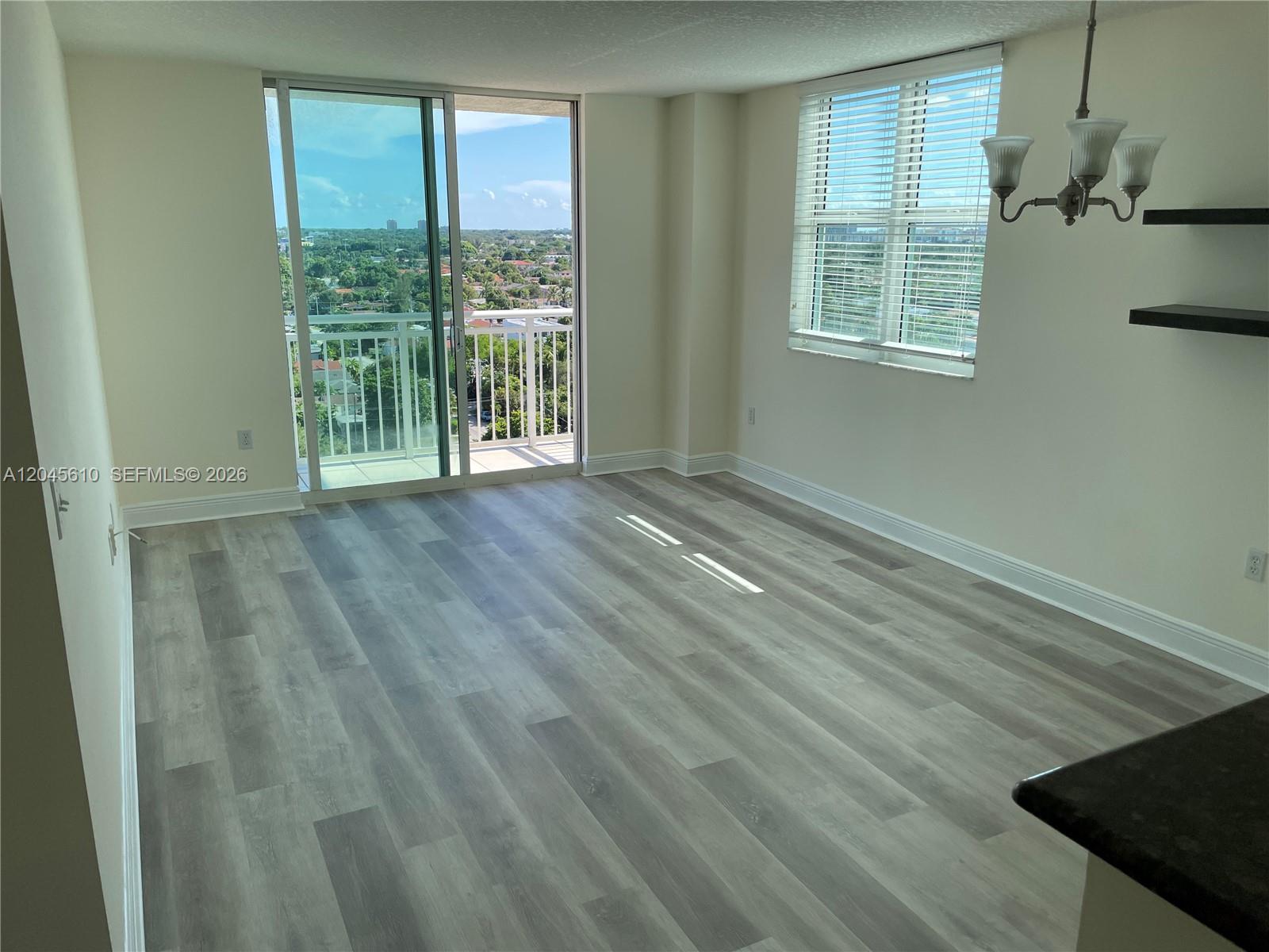 An empty room features light wood-look flooring, a sliding glass door to a balcony, and windows — 3000 Coral Way # 1402, Miami FL 33145, MIAMI, FL