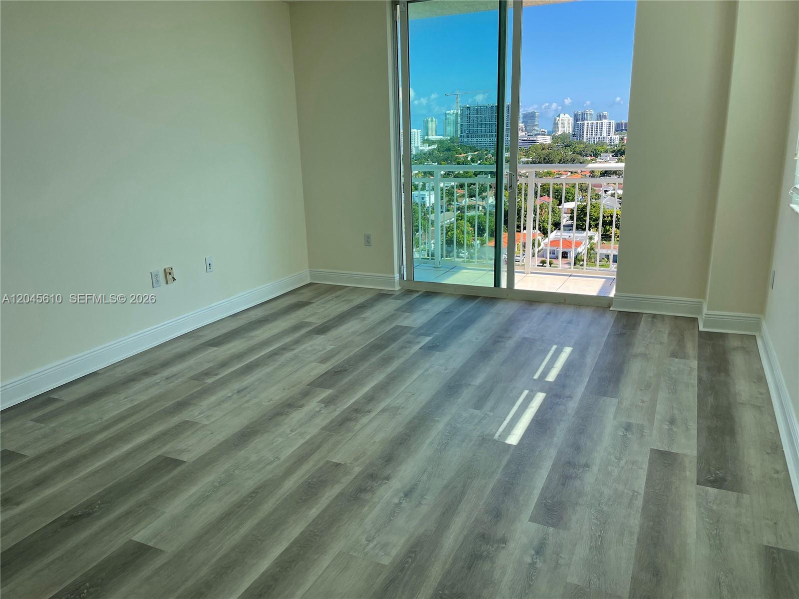 An empty room features wood-look flooring, light walls, and a sliding glass door to a balcony — 3000 Coral Way # 1402, Miami FL 33145, MIAMI, FL