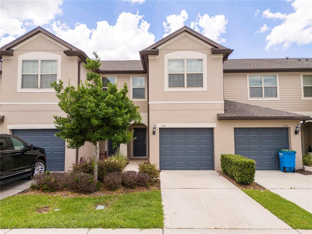 A row of two-story townhouses features beige stucco siding, dark blue garage doors, and driveways — 519 VIRTUOSO LANE UNIT 77, ORLANDO, FL