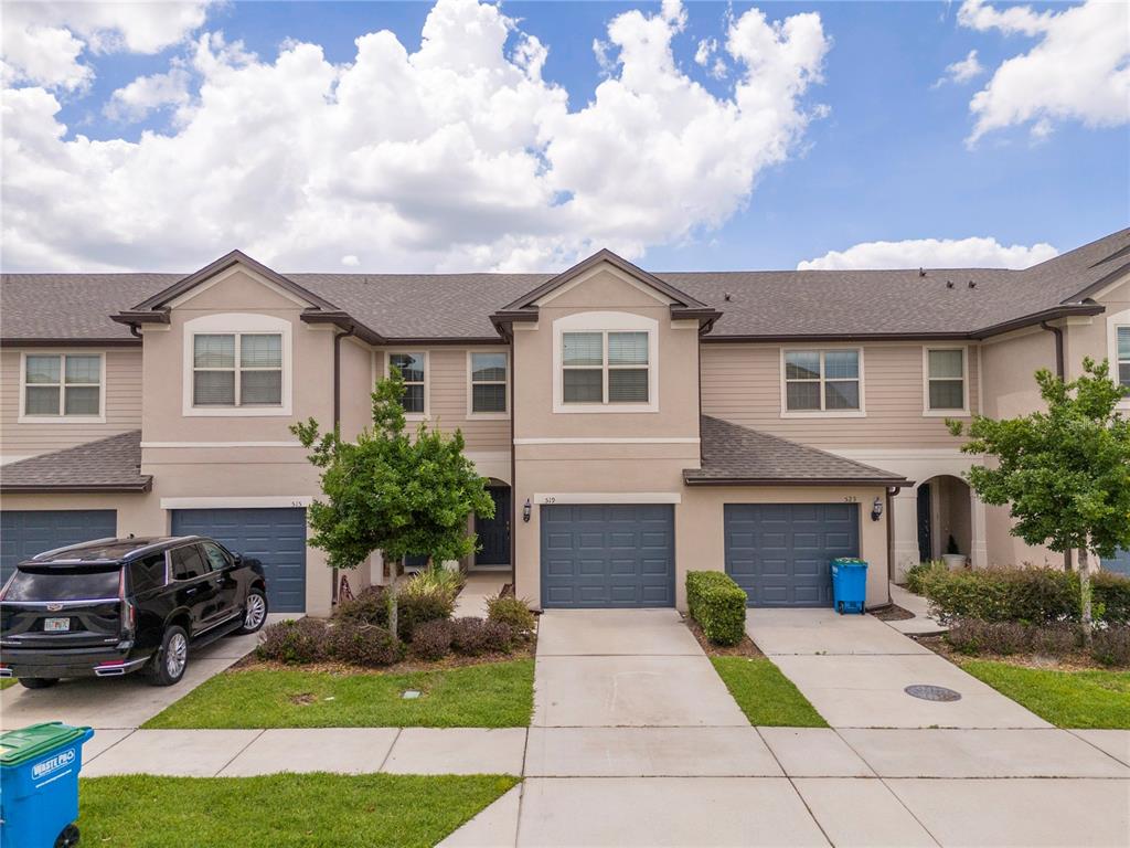 A row of three-story townhomes with beige siding, gray garage doors, and concrete driveways — 519 VIRTUOSO LANE UNIT 77, ORLANDO, FL