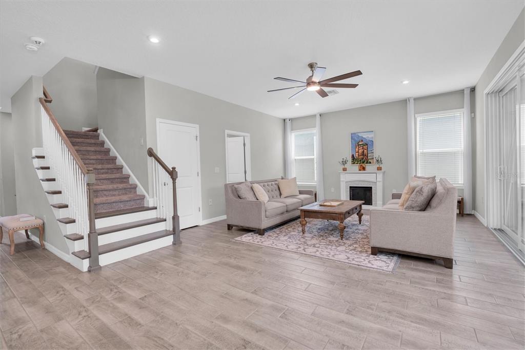 A living room features a staircase, a fireplace, two sofas, and light wood-look tile flooring — 13709 STANSIL AVENUE, ODESSA, FL