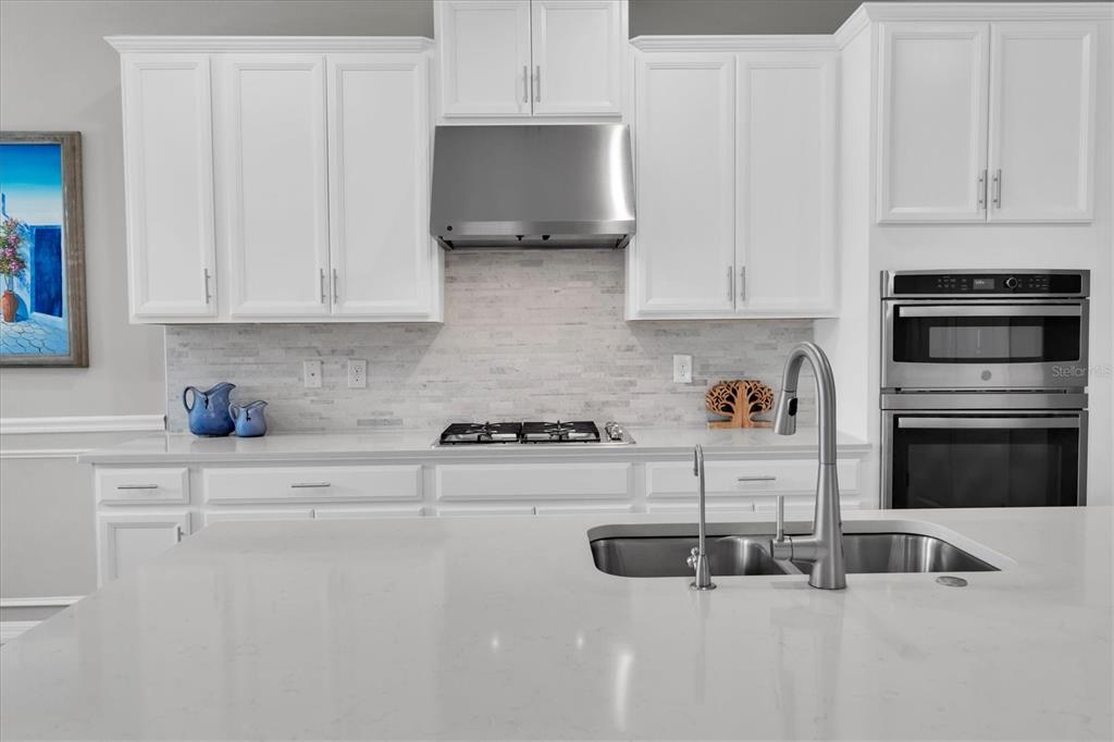 A modern kitchen features white cabinets, a stainless steel range hood, and a large island — 13709 STANSIL AVENUE, ODESSA, FL