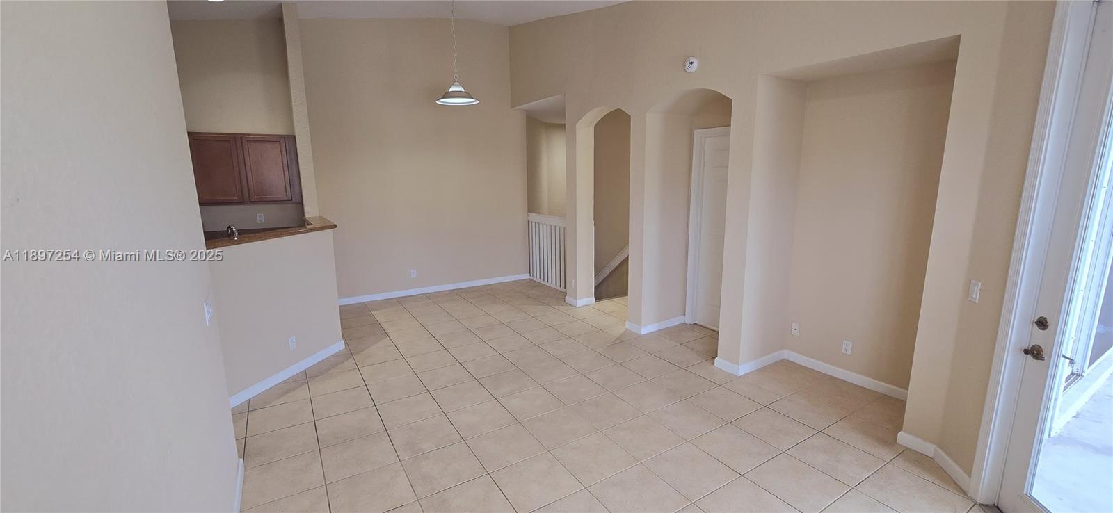 An empty room with beige tile flooring, a kitchen pass-through, and arched doorways — 3020 Laurel Ridge Cir, Riviera Beach FL 33404, RIVIERA BEACH, FL