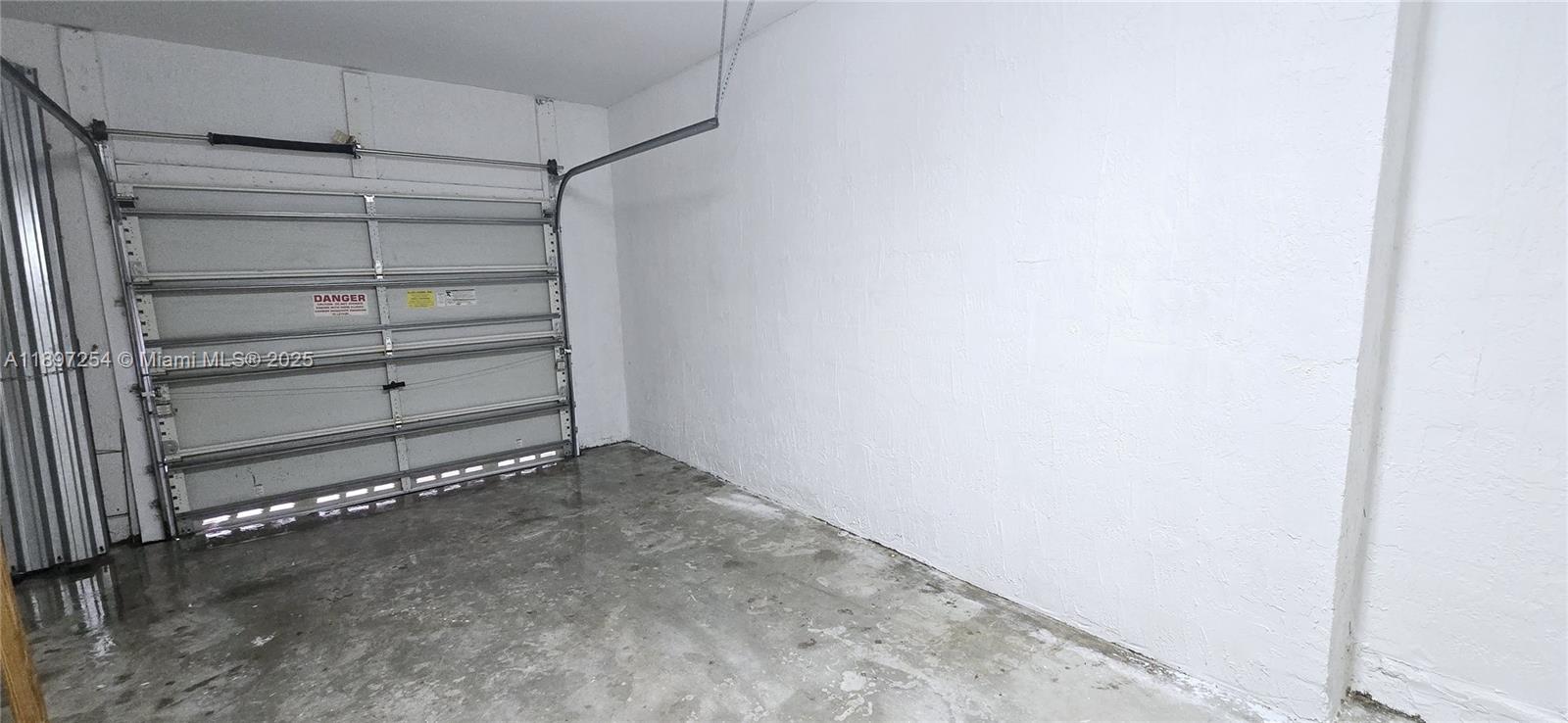 An empty garage features a white sectional door, white walls, and a concrete floor — 3020 Laurel Ridge Cir, Riviera Beach FL 33404, RIVIERA BEACH, FL