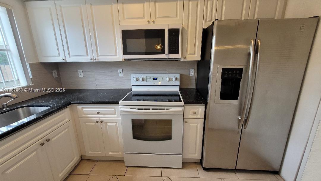A kitchen features white cabinets, black countertops, a white stove, and a stainless steel refrigerator — 8453 NW 4th Ct # 8453, Miami FL 33150, MIAMI, FL