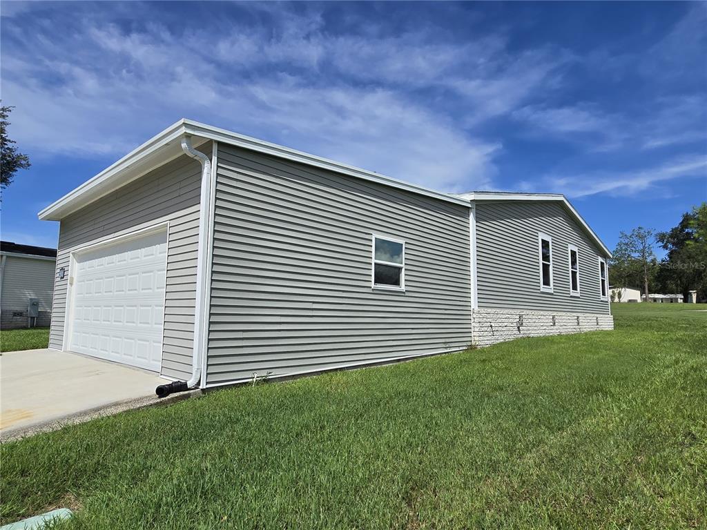 A side view of a gray vinyl-sided house with a white garage door and lawn — 4121 GREENBLUFF ROAD UNIT 1895, ZELLWOOD, FL