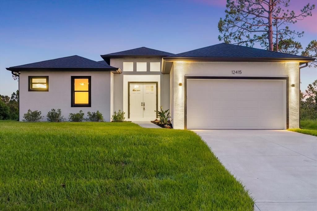 A single-story house with white stucco walls, a dark roof, and a two-car garage — 12415 MELLON AVENUE, PORT CHARLOTTE, FL