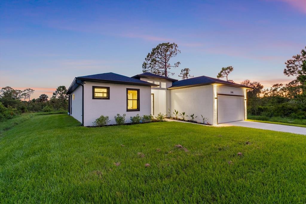 A modern, white single-story house with a two-car garage sits on a grassy lot — 12415 MELLON AVENUE, PORT CHARLOTTE, FL