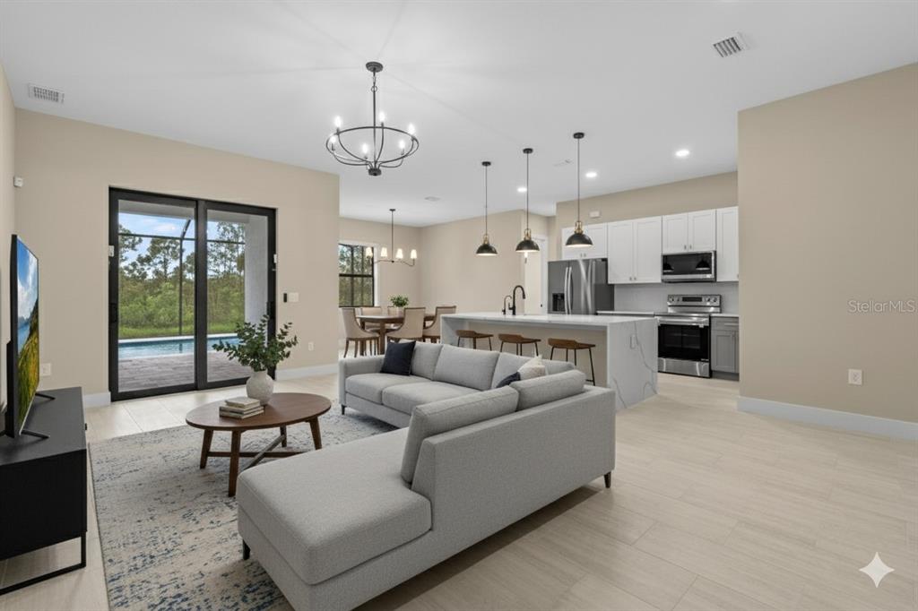 An open-concept living room and kitchen featuring a grey sectional, island seating, and sliding glass doors — 12415 MELLON AVENUE, PORT CHARLOTTE, FL