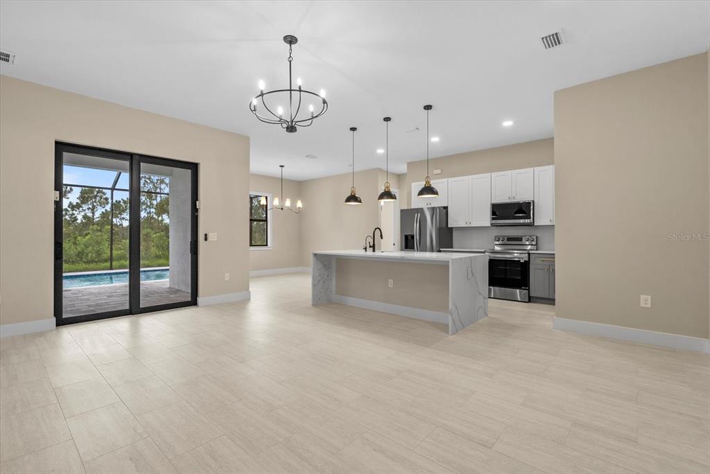 An open-concept kitchen and living area features a marble-topped island, pendant lighting, and sliding doors — 12415 MELLON AVENUE, PORT CHARLOTTE, FL