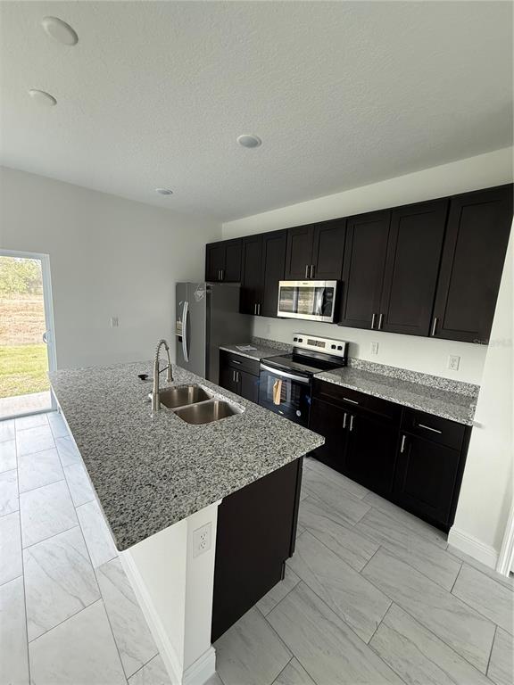 A modern kitchen features dark cabinetry, a granite-topped island with a sink, and light flooring — 2885 W REDGATE DRIVE, DUNNELLON, FL