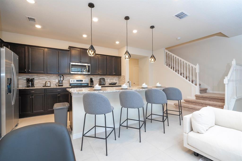 A kitchen with dark cabinets, granite countertops, and a breakfast bar with four gray stools — 4178 LANA AVENUE, DAVENPORT, FL