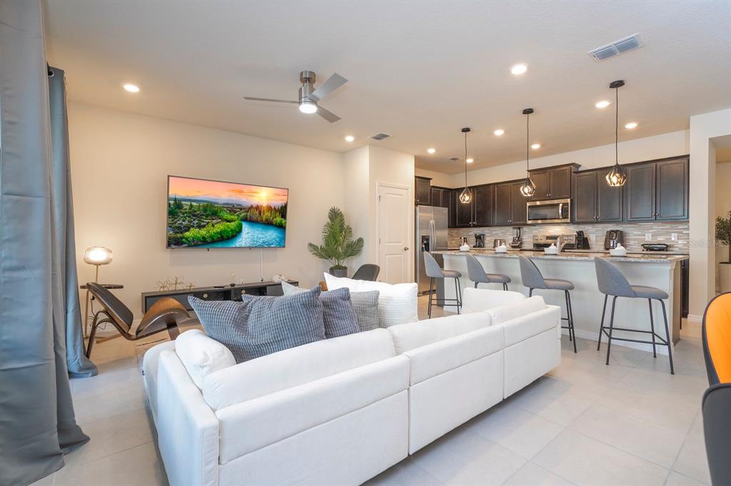 A white sectional sofa faces a wall-mounted television in an open-concept living room and kitchen — 4178 LANA AVENUE, DAVENPORT, FL