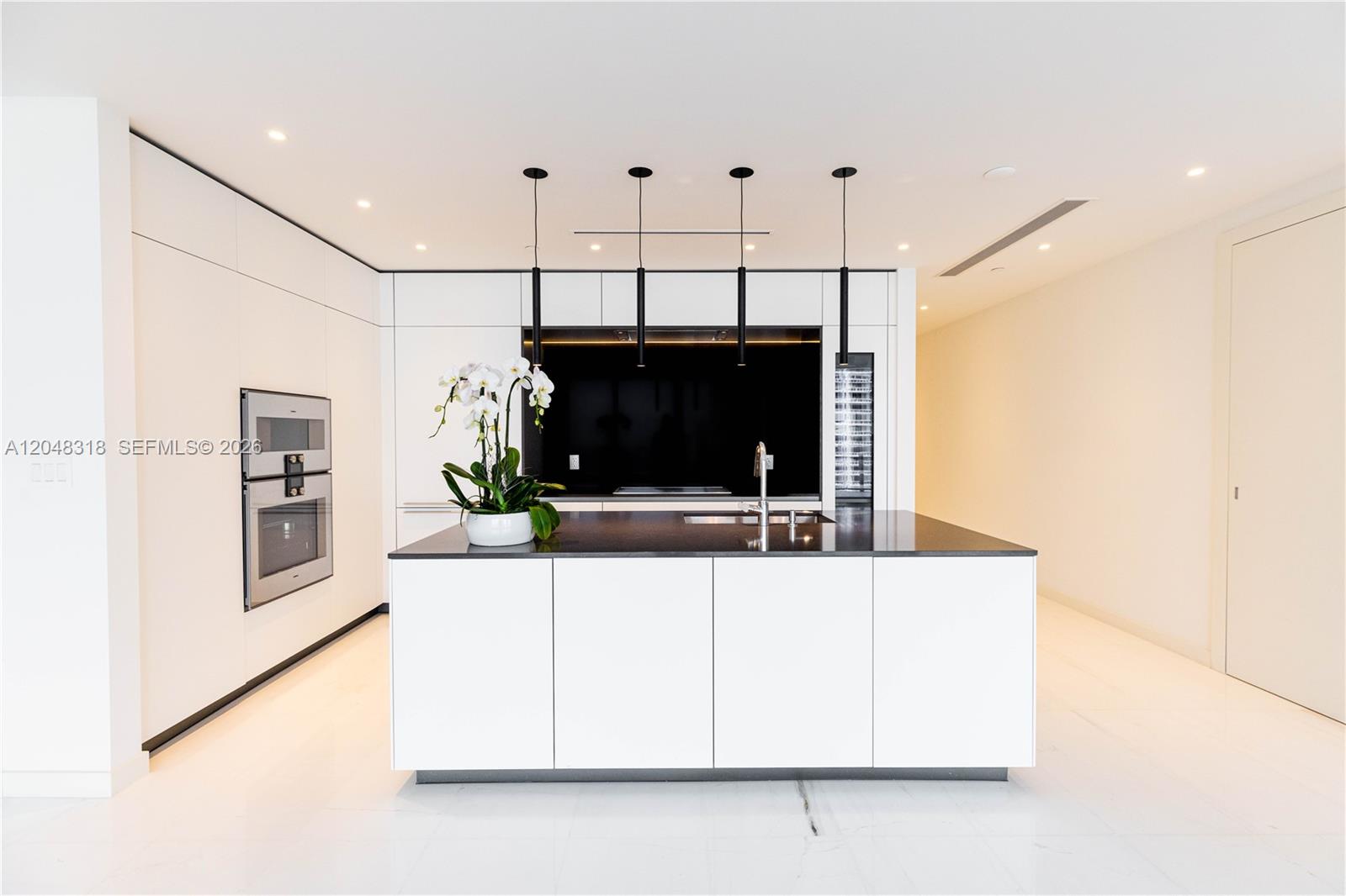 A modern kitchen features white cabinetry, a black island countertop, and four pendant lights — 300 Biscayne Blvd Way # 2702, Miami FL 33131, MIAMI, FL