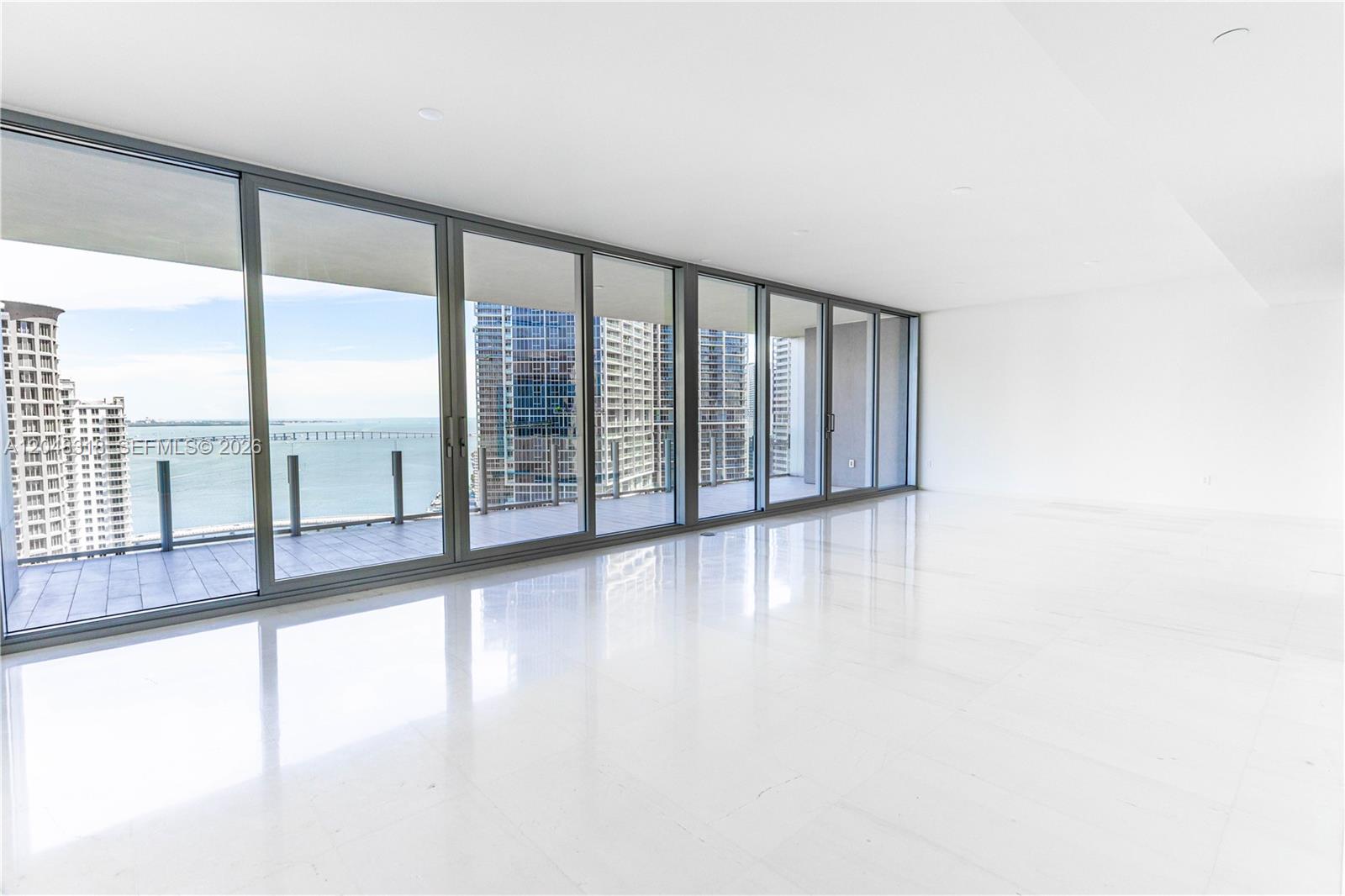 A bright, empty room features white tile floors, floor-to-ceiling windows, and a balcony overlooking water — 300 Biscayne Blvd Way # 2702, Miami FL 33131, MIAMI, FL