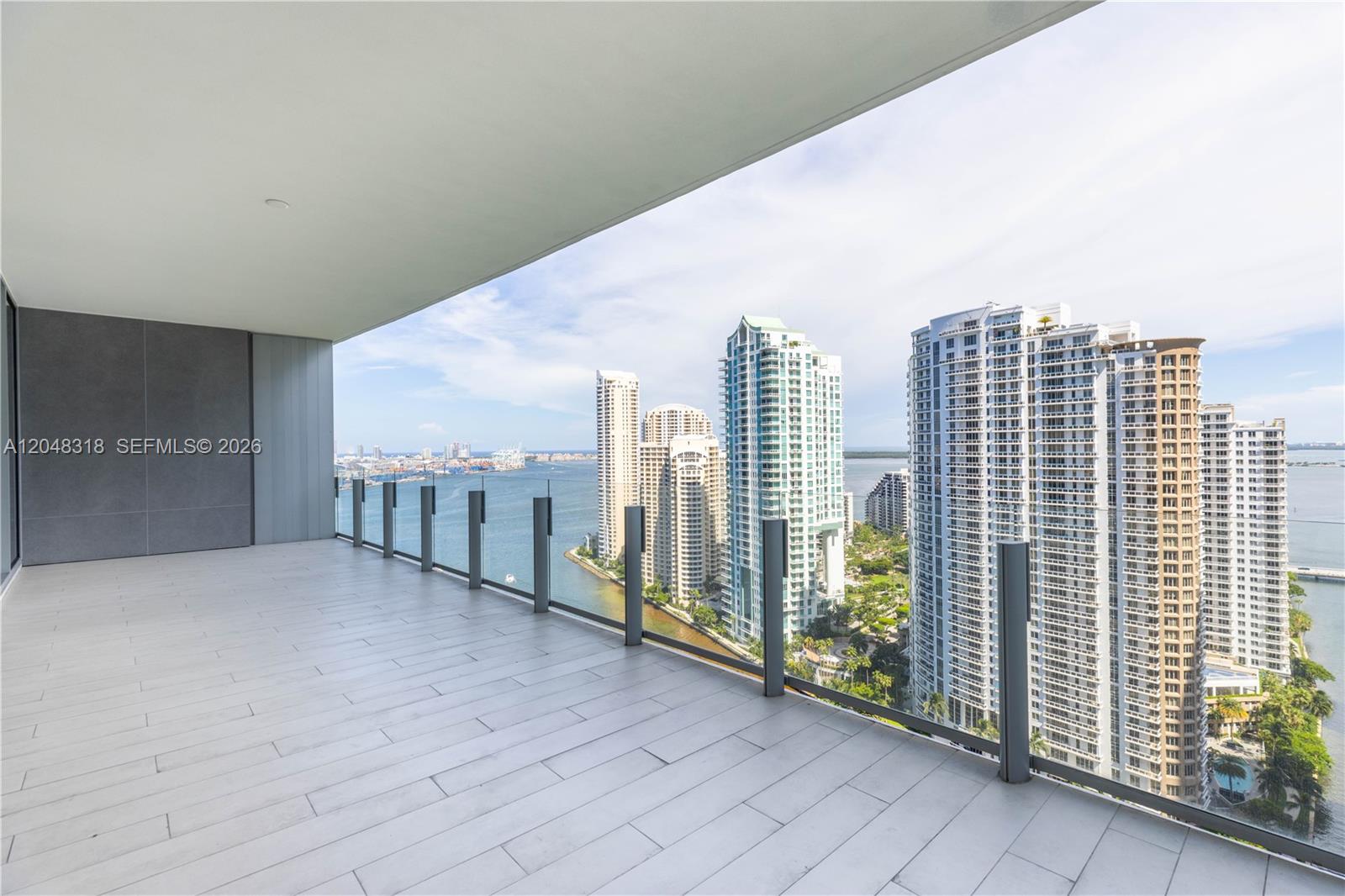 A spacious balcony with light-colored tile flooring overlooks a bay and city skyline — 300 Biscayne Blvd Way # 2702, Miami FL 33131, MIAMI, FL
