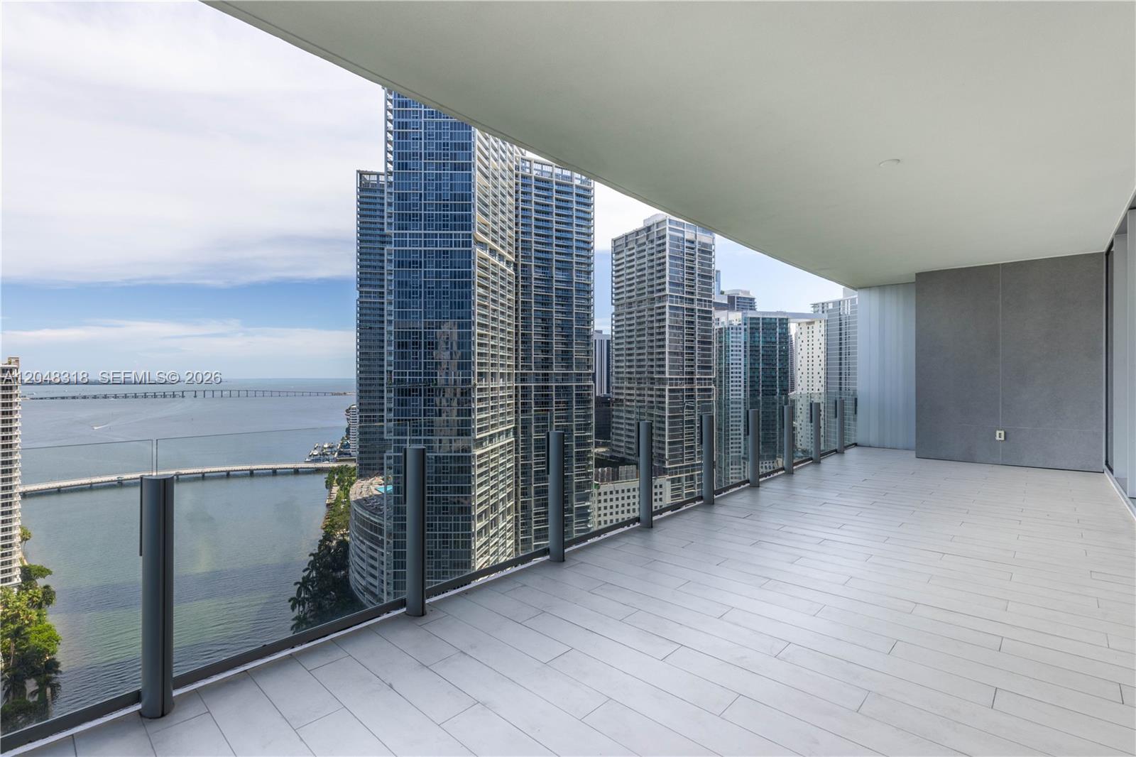 A spacious balcony features light-colored tile flooring, a glass railing, and views of city skyscrapers — 300 Biscayne Blvd Way # 2702, Miami FL 33131, MIAMI, FL
