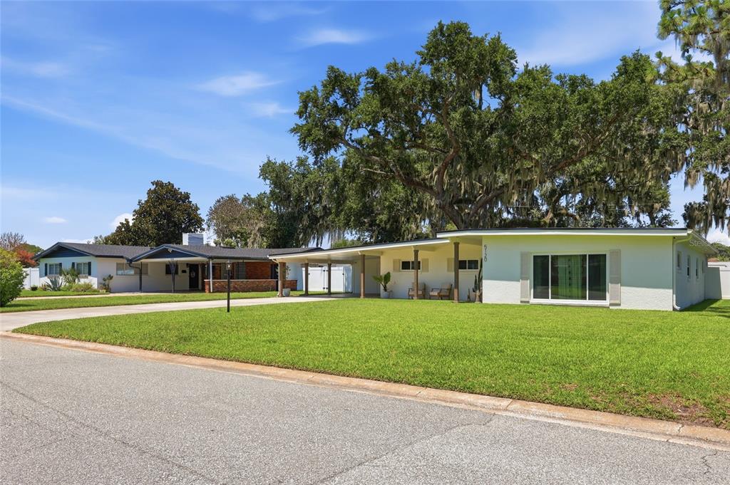 A single-story house with a carport and large oak trees sits on a grassy lot — 5120 MORTIER AVENUE, BELLE ISLE, FL